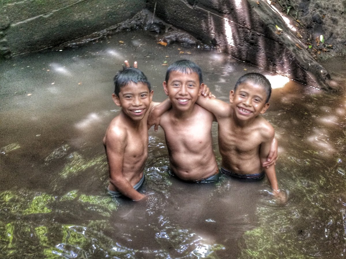 Three children smiling together in a community water source